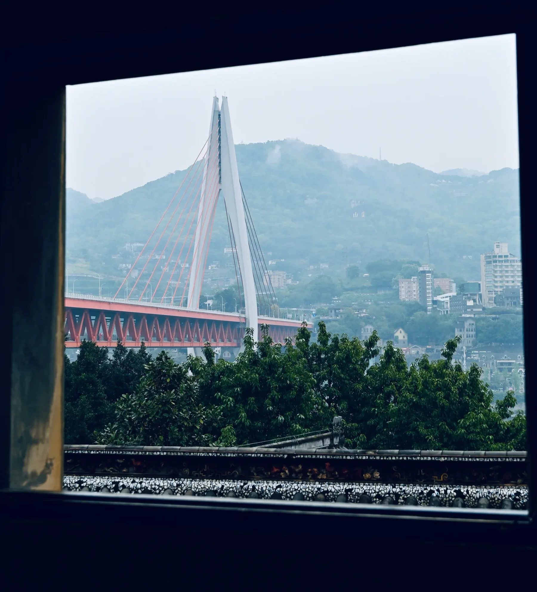 A cable-stayed bridge and a green hillside framed by a dark window.