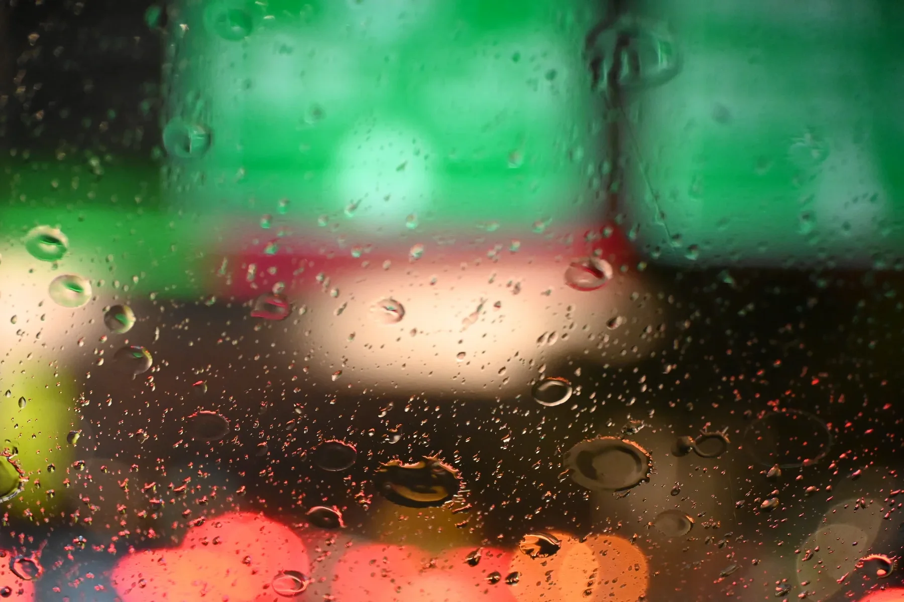 Raindrops on a window with green and red lights blurred behind them.